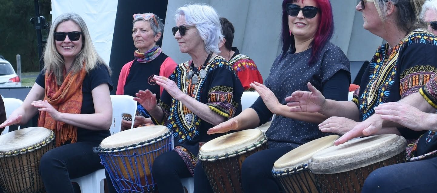 Smiling drummers in colourful African print shirts playing djembes at an outdoor festival